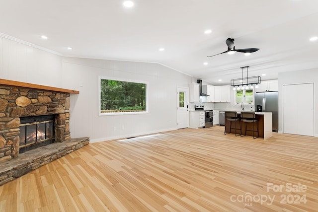 unfurnished living room with ceiling fan, vaulted ceiling, a stone fireplace, and light hardwood / wood-style flooring