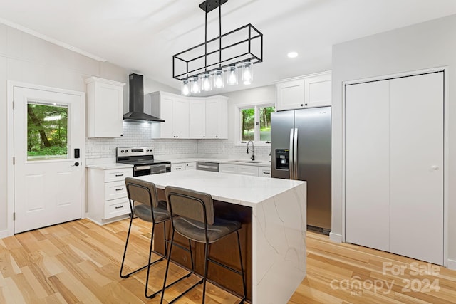 kitchen featuring stainless steel appliances, light hardwood / wood-style floors, wall chimney exhaust hood, pendant lighting, and white cabinets