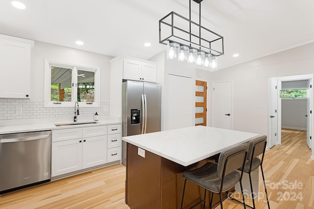 kitchen with light hardwood / wood-style flooring, a kitchen island, vaulted ceiling, appliances with stainless steel finishes, and sink