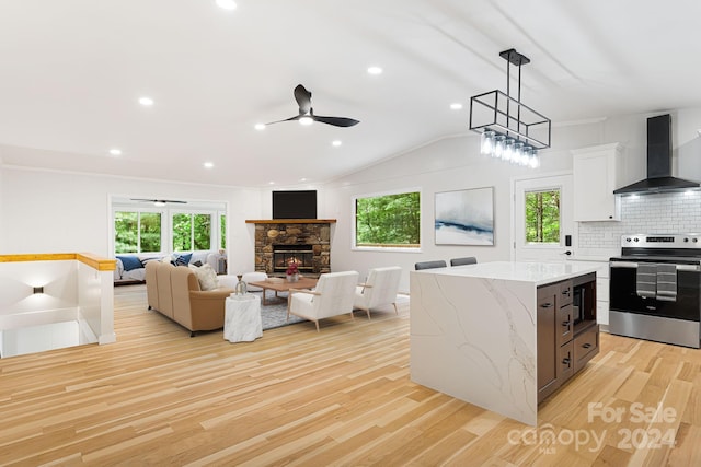 kitchen with wall chimney range hood, pendant lighting, light hardwood / wood-style floors, stainless steel range with electric stovetop, and a fireplace