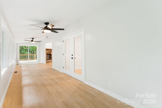 spare room featuring ceiling fan, a stone fireplace, and light hardwood / wood-style flooring