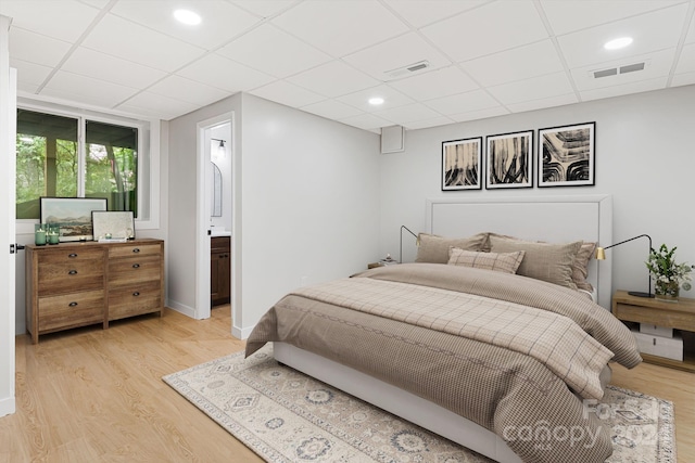 bedroom featuring light wood-type flooring, a drop ceiling, and ensuite bath