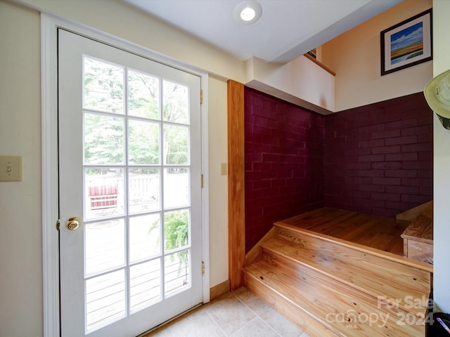 entryway with brick wall, a healthy amount of sunlight, and light tile patterned floors