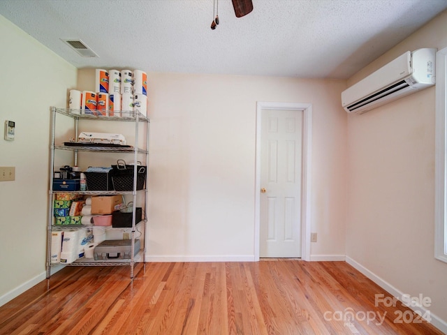 interior space with ceiling fan, hardwood / wood-style flooring, a wall mounted air conditioner, and a textured ceiling