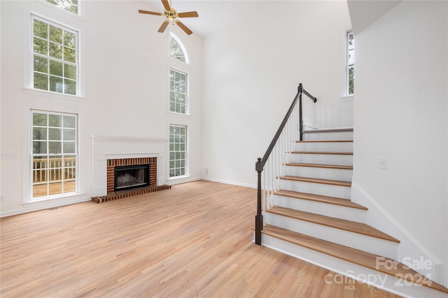 staircase with hardwood / wood-style flooring, plenty of natural light, a brick fireplace, and a towering ceiling