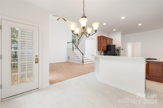 kitchen with pendant lighting, black refrigerator, kitchen peninsula, an inviting chandelier, and light tile patterned flooring