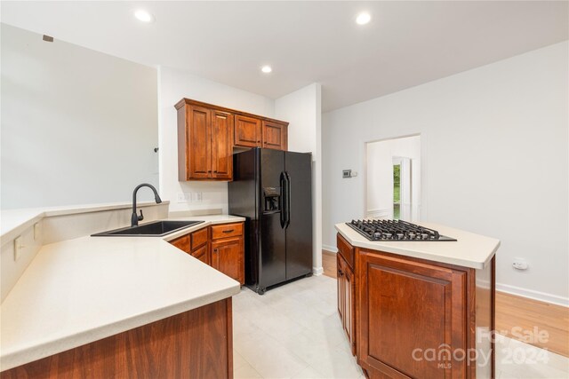 kitchen featuring sink, stainless steel gas cooktop, light tile patterned floors, kitchen peninsula, and black refrigerator with ice dispenser