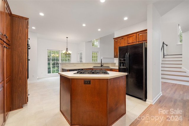 kitchen featuring sink, light wood-type flooring, kitchen peninsula, black refrigerator with ice dispenser, and pendant lighting