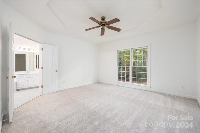 empty room featuring light colored carpet, a raised ceiling, and ceiling fan