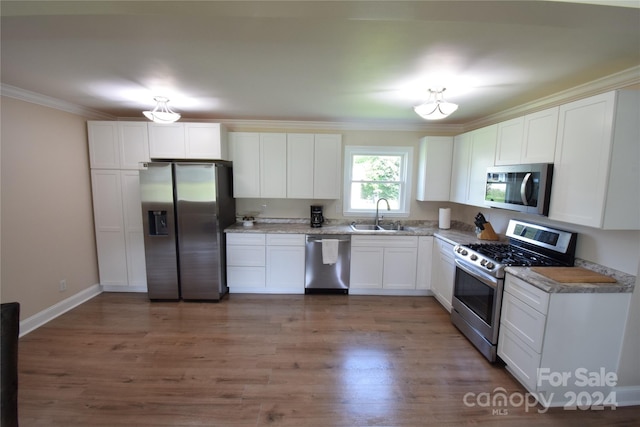 kitchen featuring crown molding, light wood-style flooring, appliances with stainless steel finishes, white cabinetry, and a sink