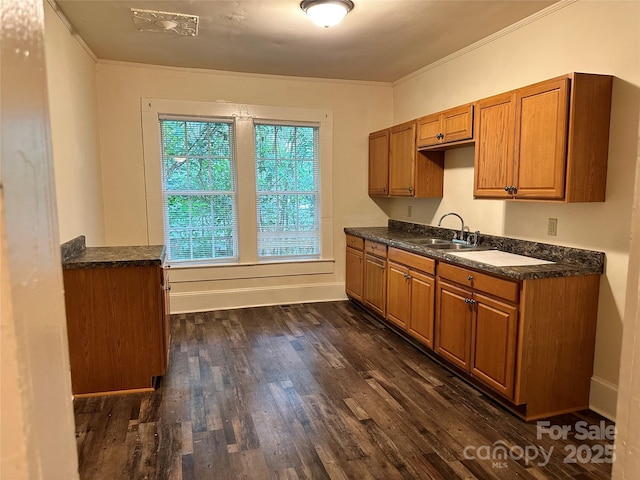 kitchen featuring dark wood-style floors, brown cabinets, crown molding, dark countertops, and a sink