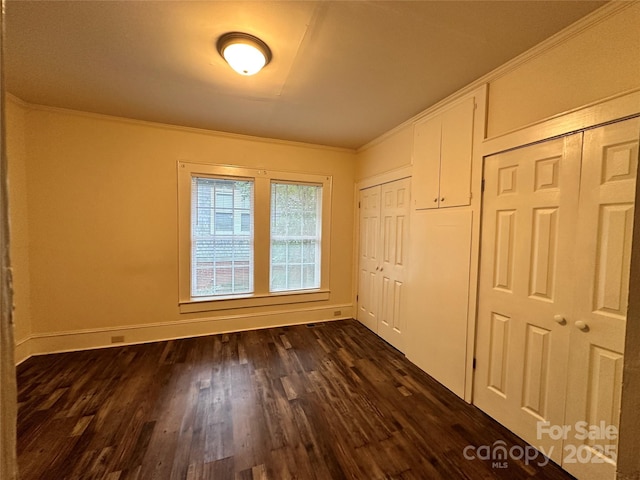 unfurnished bedroom featuring ornamental molding, dark wood-style flooring, and baseboards