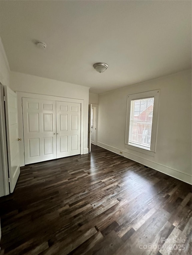 unfurnished bedroom with dark wood-style flooring, a closet, and baseboards