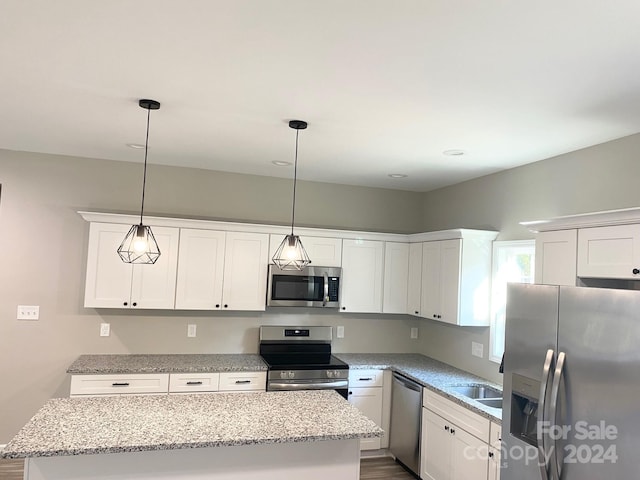 kitchen with appliances with stainless steel finishes, white cabinets, a kitchen island, and decorative light fixtures