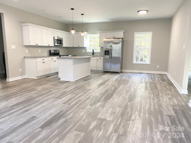 kitchen featuring light stone countertops, white cabinets, appliances with stainless steel finishes, a center island, and pendant lighting