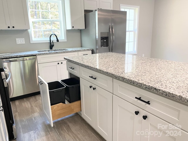 kitchen with white cabinets, appliances with stainless steel finishes, wood finished floors, light stone countertops, and a sink