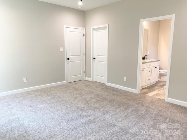 unfurnished bedroom featuring connected bathroom, light carpet, a sink, and baseboards