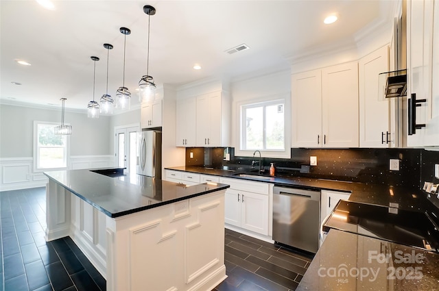 kitchen with appliances with stainless steel finishes, ornamental molding, a kitchen island, white cabinetry, and hanging light fixtures