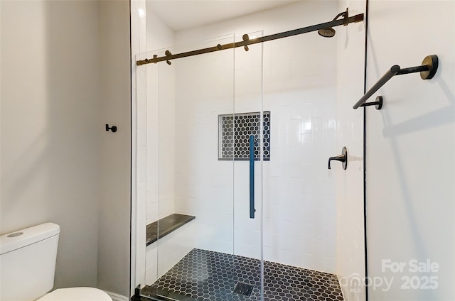 bathroom featuring a shower with door and toilet