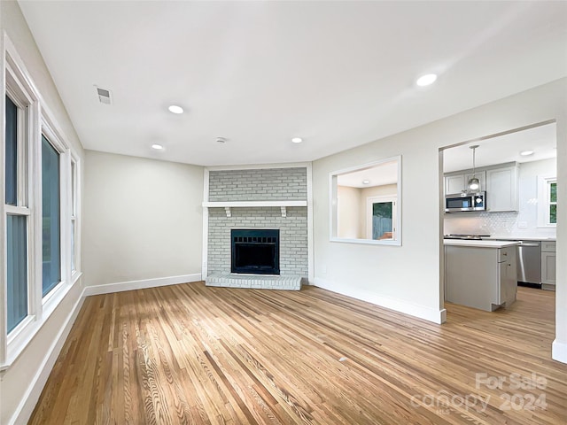 unfurnished living room featuring a brick fireplace and light hardwood / wood-style flooring