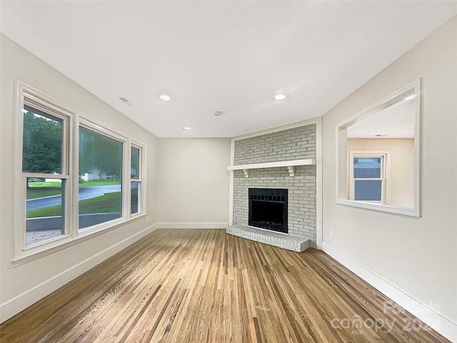 unfurnished living room with wood-type flooring, brick wall, and a brick fireplace