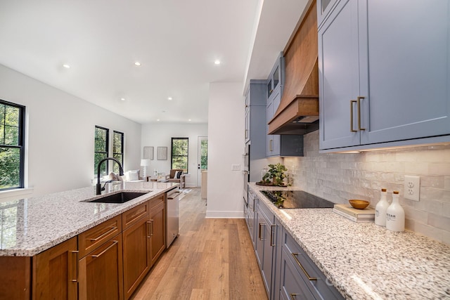 kitchen with tasteful backsplash, light hardwood / wood-style floors, light stone countertops, black electric cooktop, and sink