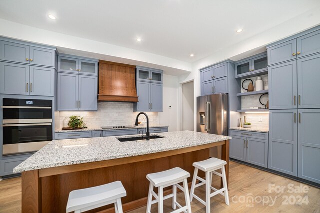 kitchen featuring custom range hood, appliances with stainless steel finishes, decorative backsplash, light stone counters, and light hardwood / wood-style floors