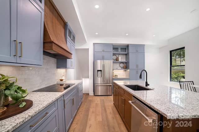 kitchen featuring stainless steel appliances, light hardwood / wood-style floors, premium range hood, sink, and an island with sink