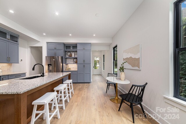 kitchen featuring light hardwood / wood-style flooring, high end refrigerator, decorative backsplash, sink, and light stone countertops