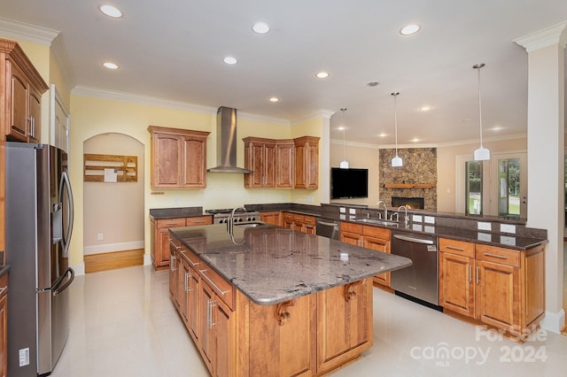 kitchen featuring stainless steel appliances, sink, wall chimney range hood, hanging light fixtures, and an island with sink