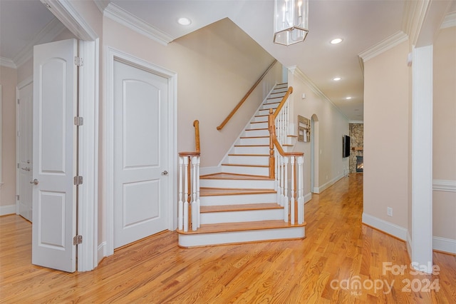 stairs featuring a stone fireplace, crown molding, a chandelier, and hardwood / wood-style flooring