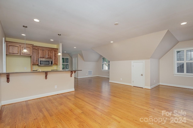 kitchen with decorative light fixtures, a healthy amount of sunlight, a kitchen bar, and light hardwood / wood-style flooring