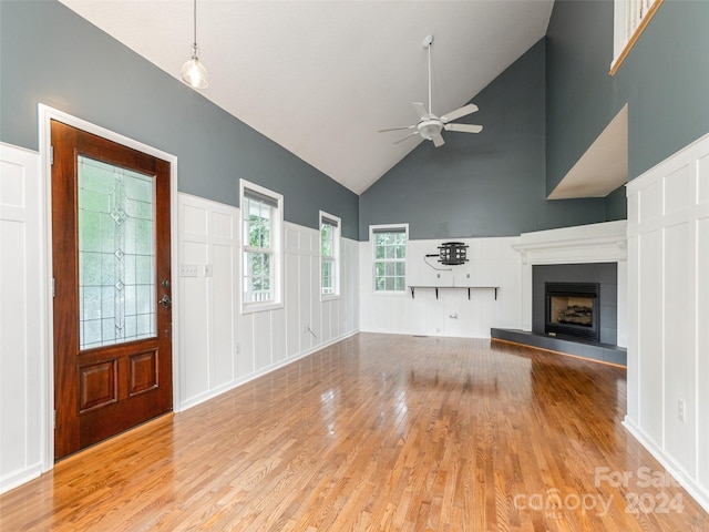 unfurnished living room featuring a tiled fireplace, high vaulted ceiling, ceiling fan, and light hardwood / wood-style floors