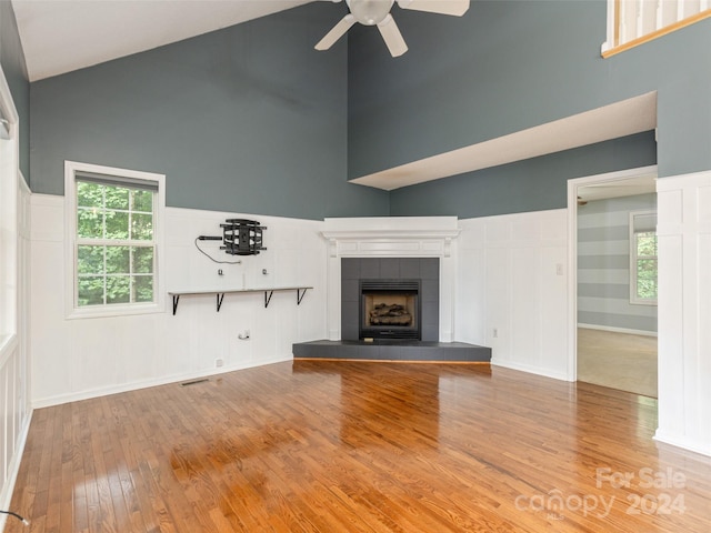 unfurnished living room with a towering ceiling, light hardwood / wood-style flooring, a tile fireplace, and ceiling fan