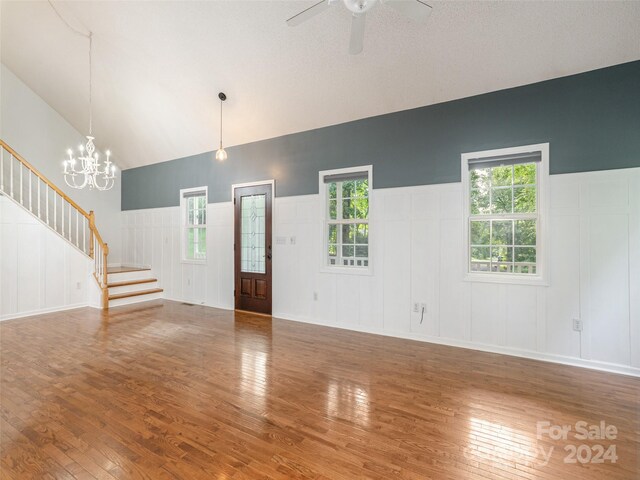 empty room with high vaulted ceiling, ceiling fan with notable chandelier, and hardwood / wood-style floors