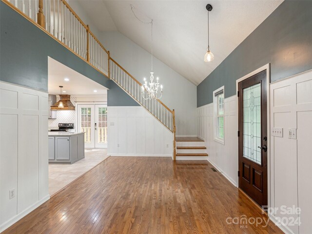 entryway with high vaulted ceiling, french doors, an inviting chandelier, and light hardwood / wood-style floors