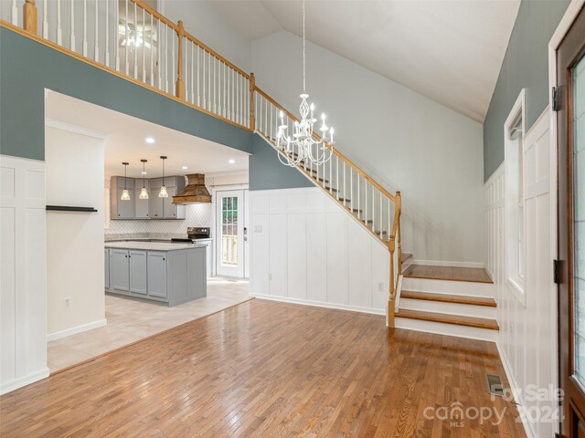 unfurnished living room with a notable chandelier, high vaulted ceiling, and light hardwood / wood-style flooring