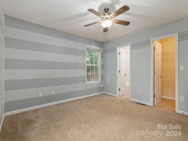 unfurnished bedroom featuring ensuite bath, light carpet, ceiling fan, a spacious closet, and a closet