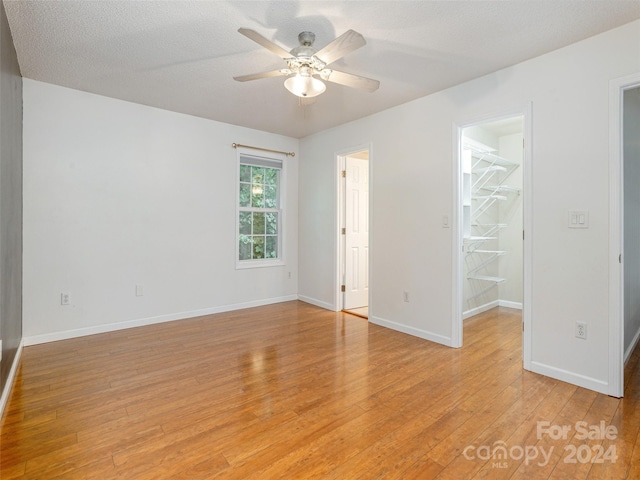 empty room with ceiling fan, light hardwood / wood-style flooring, and a textured ceiling