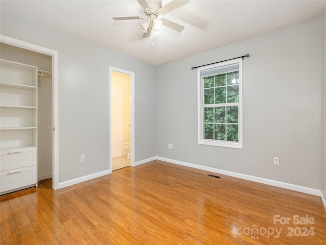 unfurnished bedroom with connected bathroom, a textured ceiling, light hardwood / wood-style floors, a spacious closet, and ceiling fan