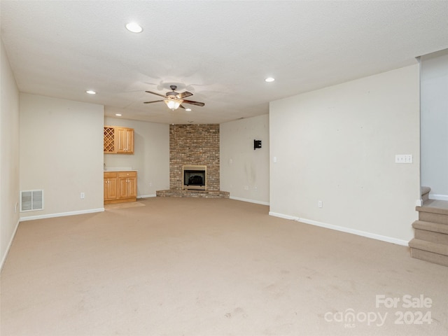 unfurnished living room featuring a fireplace, a textured ceiling, ceiling fan, light colored carpet, and brick wall