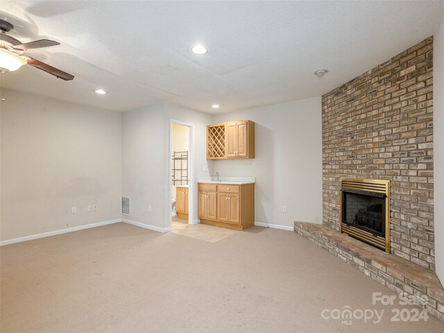 unfurnished living room featuring a textured ceiling, light colored carpet, ceiling fan, sink, and a fireplace