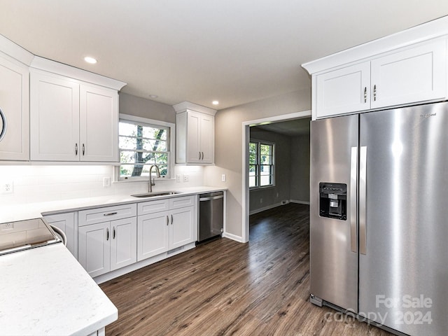 kitchen with appliances with stainless steel finishes, white cabinets, wood-type flooring, sink, and backsplash