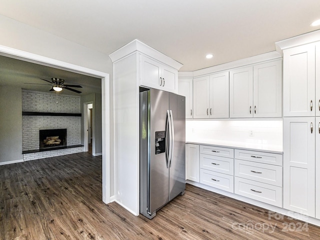 kitchen featuring hardwood / wood-style floors, white cabinetry, stainless steel fridge, brick wall, and a brick fireplace