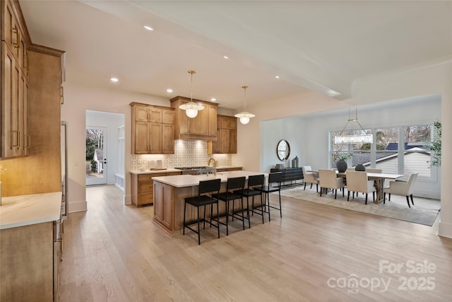 kitchen featuring a center island, beam ceiling, pendant lighting, decorative backsplash, and light wood-type flooring