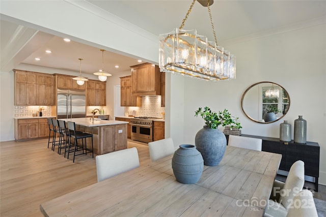 dining space with sink, an inviting chandelier, ornamental molding, and light hardwood / wood-style flooring