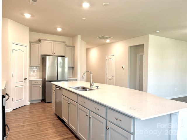 kitchen with gray cabinetry, a center island with sink, sink, decorative backsplash, and stainless steel appliances