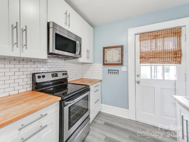 kitchen with appliances with stainless steel finishes, butcher block counters, white cabinets, and decorative backsplash