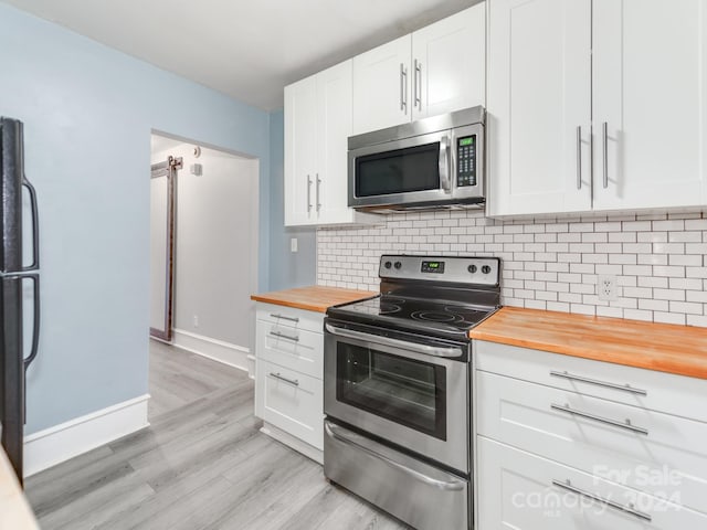 kitchen with appliances with stainless steel finishes, white cabinetry, butcher block counters, decorative backsplash, and light hardwood / wood-style floors