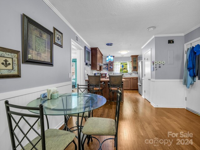 dining space with crown molding, a textured ceiling, and light hardwood / wood-style floors